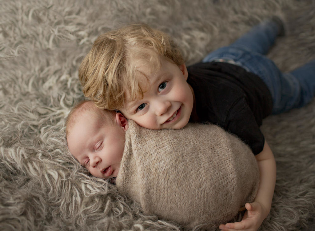 big brother snuggling his swaddled newborn brother