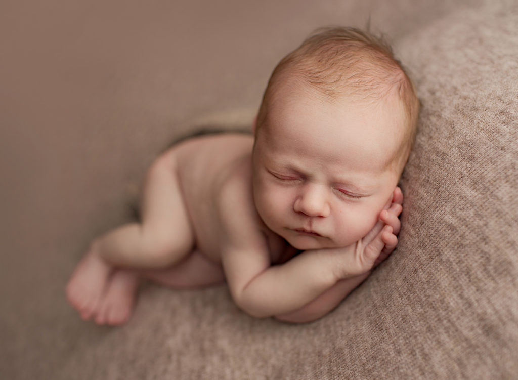 Neutral toned image of newborn baby boy side sleeping